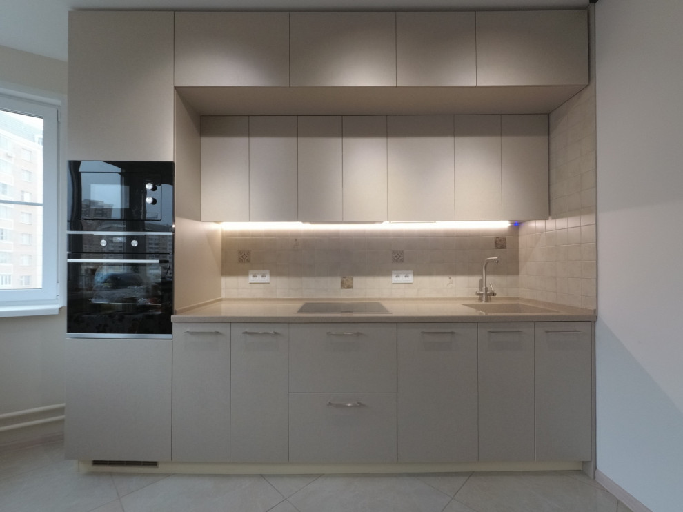 Inspiration for a small contemporary single-wall porcelain tile and beige floor enclosed kitchen remodel in Moscow with an integrated sink, flat-panel cabinets, beige cabinets, solid surface countertops, beige backsplash, ceramic backsplash, black appliances, no island and beige countertops