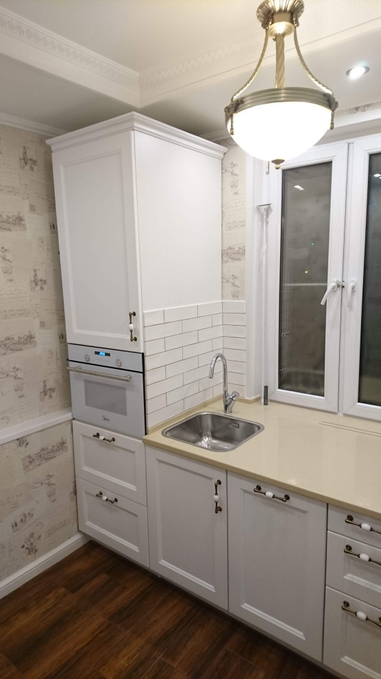 Imagen de cocina actual pequeña con fregadero encastrado, armarios con paneles empotrados, puertas de armario blancas, encimera de acrílico, salpicadero blanco, salpicadero de azulejos tipo metro, electrodomésticos blancos, suelo de baldosas de terracota, suelo marrón, encimeras beige y bandeja