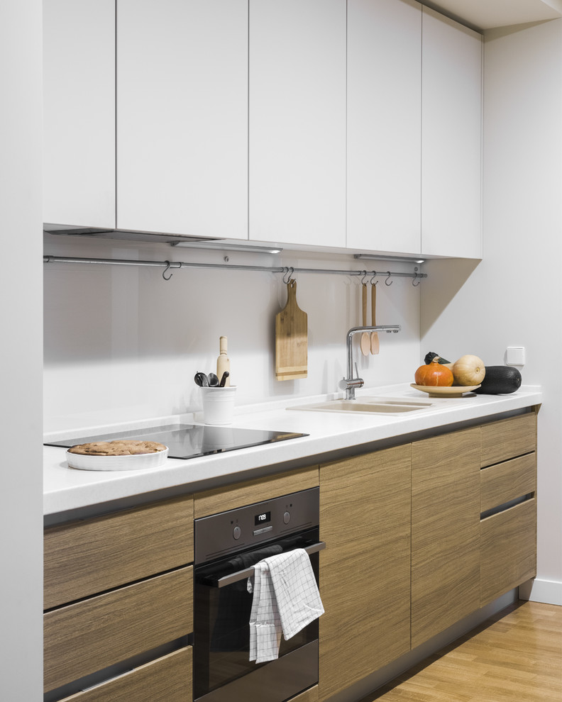 Inspiration for a medium sized scandinavian kitchen in Moscow with flat-panel cabinets, light wood cabinets, a built-in sink, engineered stone countertops, white splashback, glass sheet splashback, stainless steel appliances, light hardwood flooring, white worktops and beige floors.