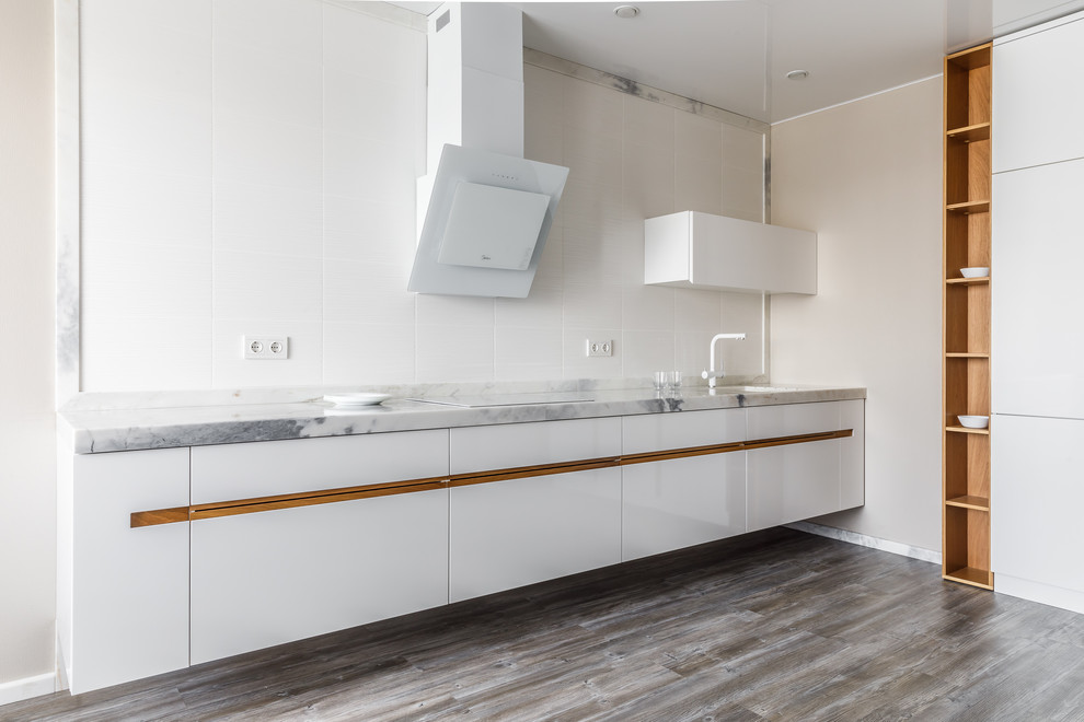 Immagine di una cucina lineare design con lavello sottopiano, ante lisce, ante bianche, top in marmo, paraspruzzi bianco, nessuna isola, pavimento marrone e top grigio
