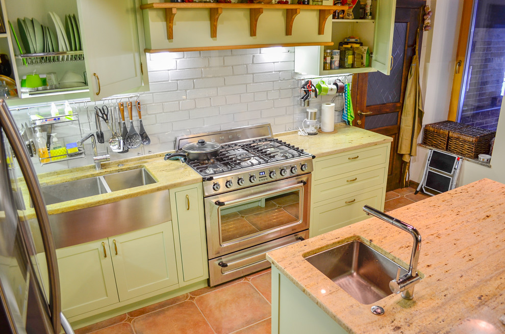 Photo of a large classic l-shaped open plan kitchen in Moscow with a double-bowl sink, shaker cabinets, green cabinets, granite worktops, white splashback, glass tiled splashback, stainless steel appliances, terracotta flooring, an island, brown floors and multicoloured worktops.