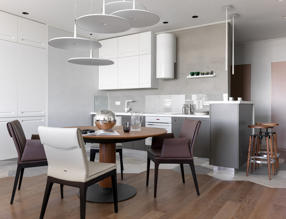 Photo of a medium sized contemporary single-wall kitchen/diner in Moscow with a built-in sink, flat-panel cabinets, grey cabinets, grey splashback, white appliances, ceramic flooring, a breakfast bar, multi-coloured floors, white worktops and glass sheet splashback.