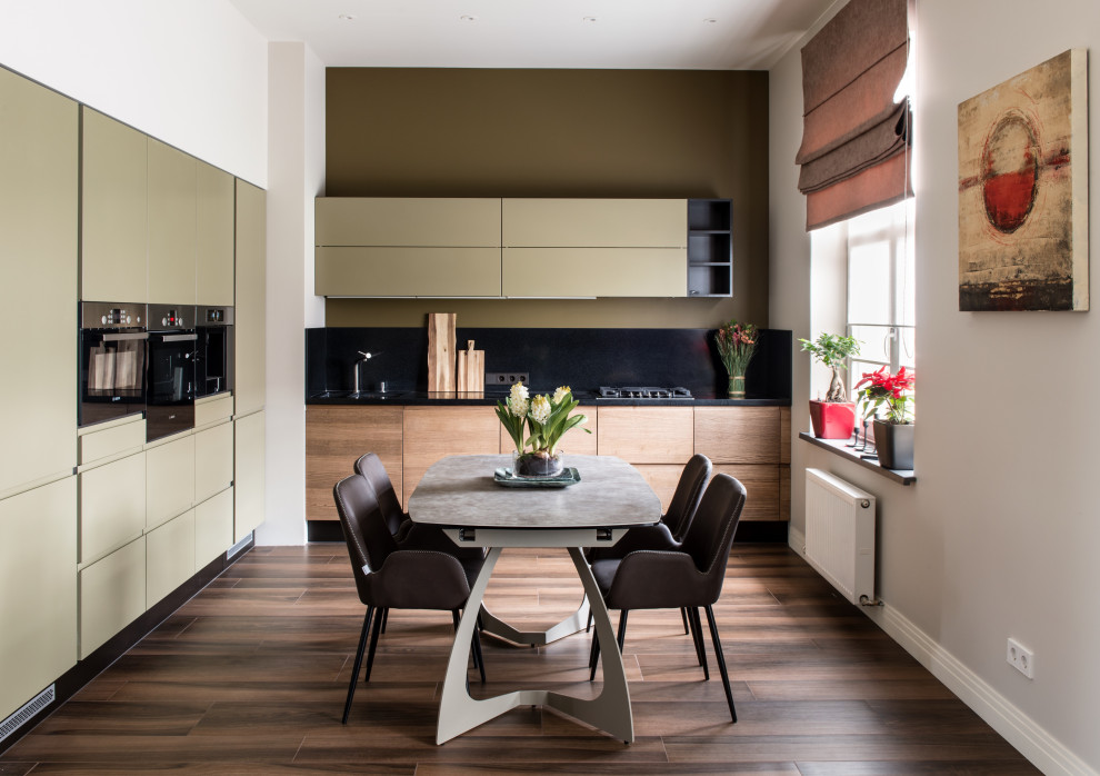 Immagine di una cucina a L contemporanea con ante lisce, ante beige, paraspruzzi nero, elettrodomestici in acciaio inossidabile, pavimento marrone e top nero