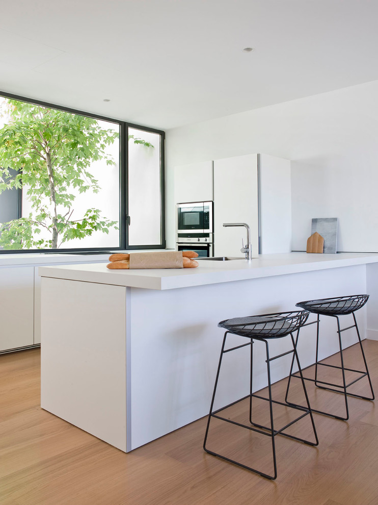 Bild på ett mellanstort minimalistiskt kök, med en undermonterad diskho, släta luckor, vita skåp, rostfria vitvaror, en halv köksö, ljust trägolv och bänkskiva i koppar