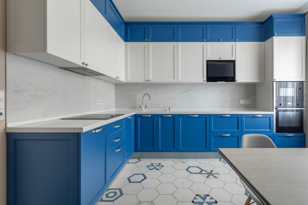 На фото: угловая кухня среднего размера в современном стиле с накладной мойкой, фасадами с утопленной филенкой, синими фасадами, белым фартуком, белой столешницей и двухцветным гарнитуром без острова