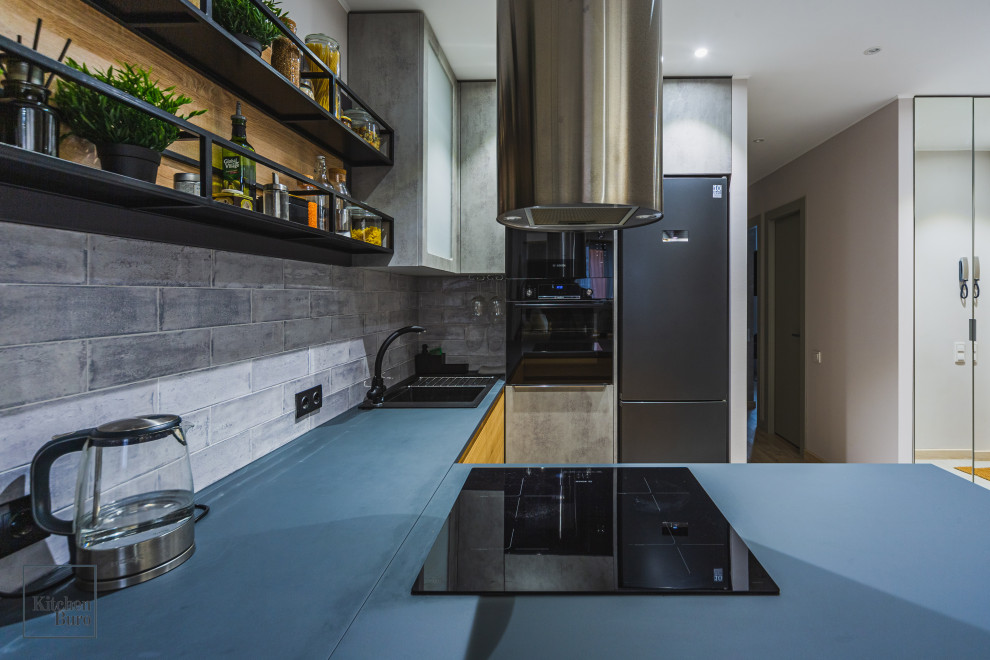 Bild på ett litet funkis blå blått u-kök, med en nedsänkt diskho, släta luckor, grå skåp, svarta vitvaror, en halv köksö, grått stänkskydd, stänkskydd i tunnelbanekakel och beiget golv