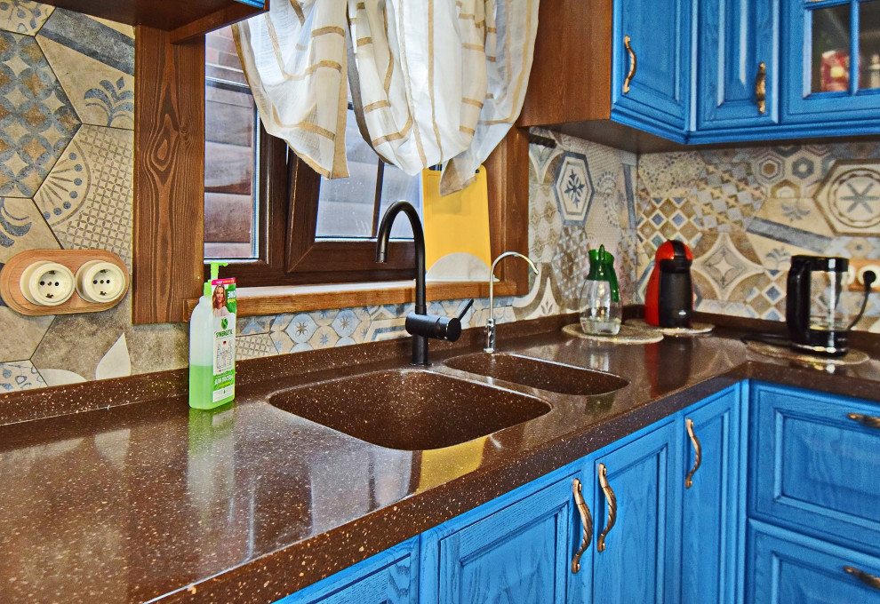 Rustik inredning av ett mellanstort brun brunt kök, med en integrerad diskho, luckor med upphöjd panel, blå skåp, bänkskiva i koppar, flerfärgad stänkskydd, stänkskydd i porslinskakel, svarta vitvaror, klinkergolv i porslin och grått golv