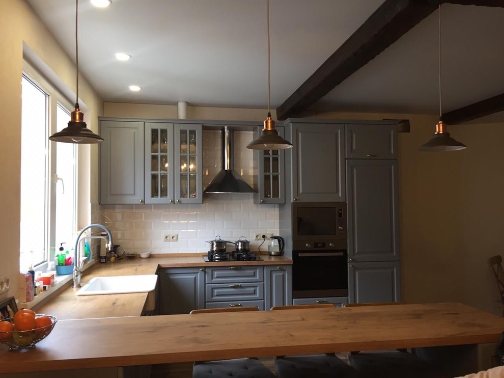 Bild på ett stort lantligt beige beige kök, med en rustik diskho, luckor med upphöjd panel, grå skåp, laminatbänkskiva, vitt stänkskydd, stänkskydd i tunnelbanekakel, rostfria vitvaror och en köksö