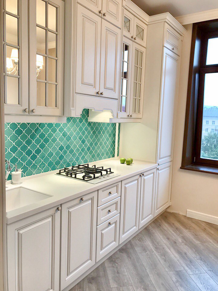Example of a small beach style single-wall laminate floor and gray floor enclosed kitchen design in Other with an undermount sink, recessed-panel cabinets, white cabinets, solid surface countertops, green backsplash, mosaic tile backsplash, white appliances, no island and white countertops