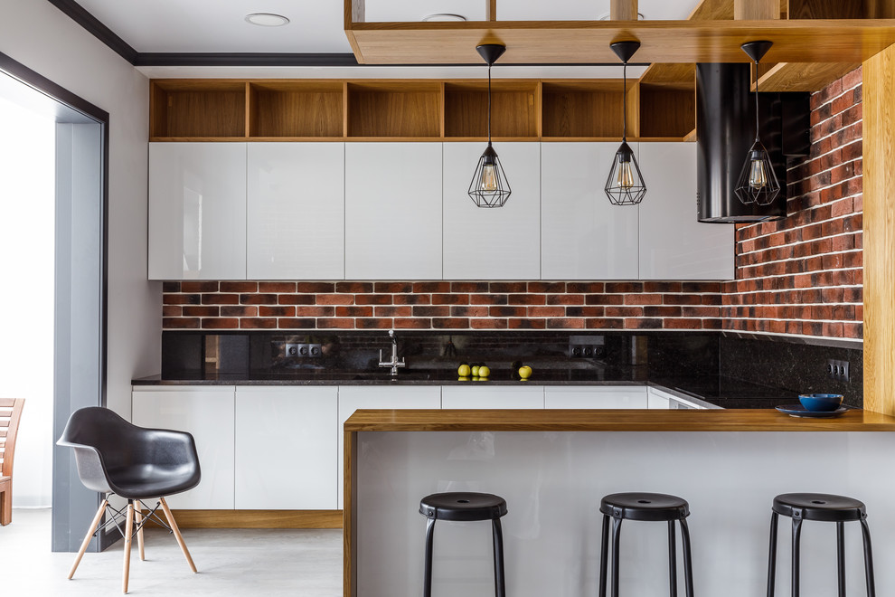 На фото: п-образная, глянцевая кухня в стиле лофт с плоскими фасадами, белыми фасадами, черным фартуком, полуостровом, серым полом и черной столешницей