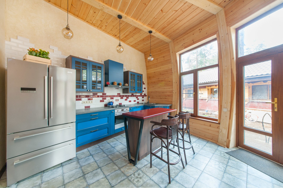На фото: параллельная кухня в современном стиле с обеденным столом, накладной мойкой, фасадами в стиле шейкер, синими фасадами, красным фартуком, фартуком из плитки кабанчик, техникой из нержавеющей стали, островом, серым полом и красной столешницей в частном доме