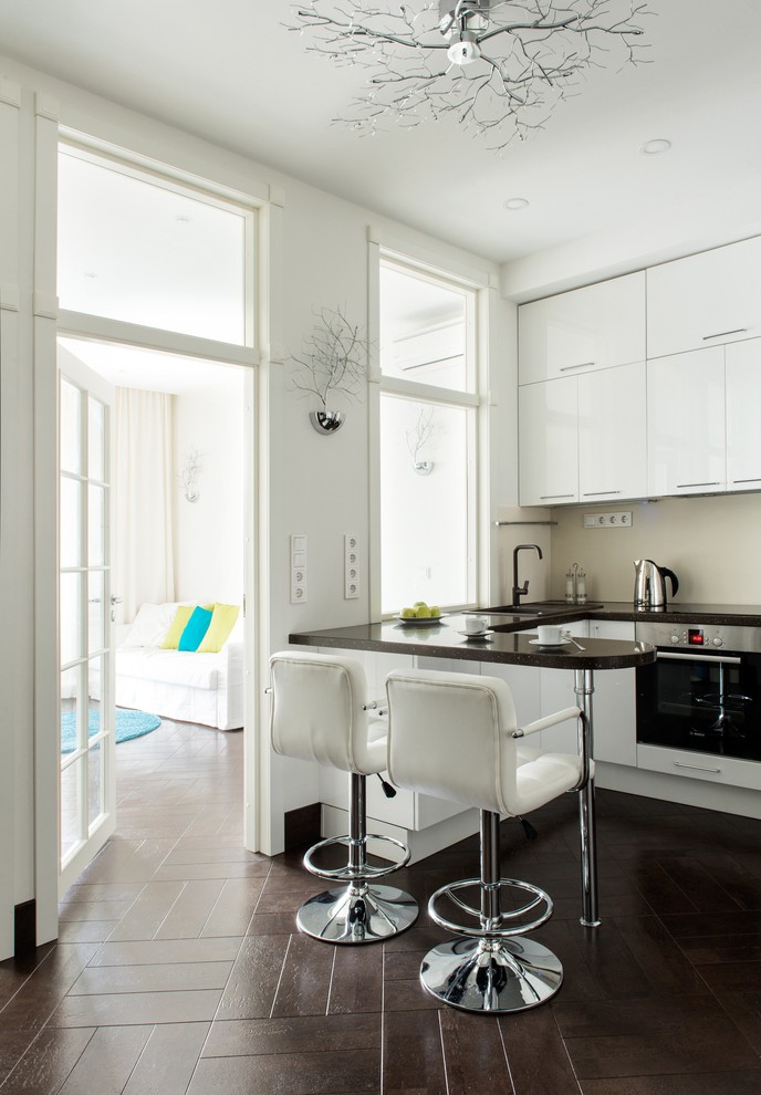 Bild på ett funkis u-kök, med en nedsänkt diskho, släta luckor, vita skåp, beige stänkskydd, rostfria vitvaror och brunt golv