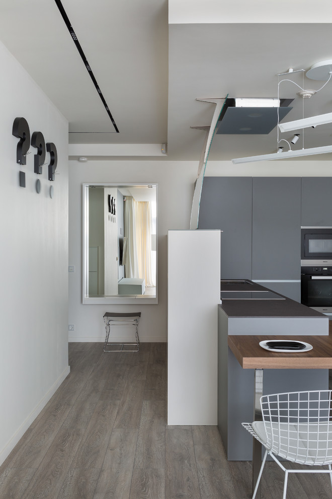 Diseño de cocina escandinava con armarios con paneles lisos, puertas de armario grises, electrodomésticos negros y suelo de madera en tonos medios
