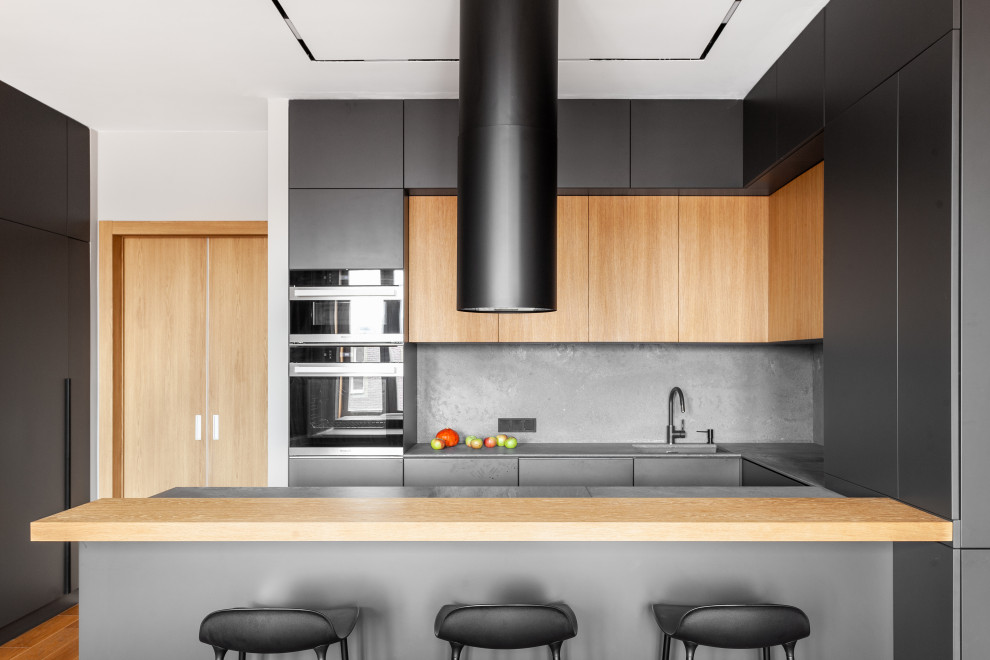На фото: п-образная кухня в современном стиле с врезной мойкой, плоскими фасадами, серыми фасадами, серым фартуком, черной техникой, полуостровом, черной столешницей и двухцветным гарнитуром
