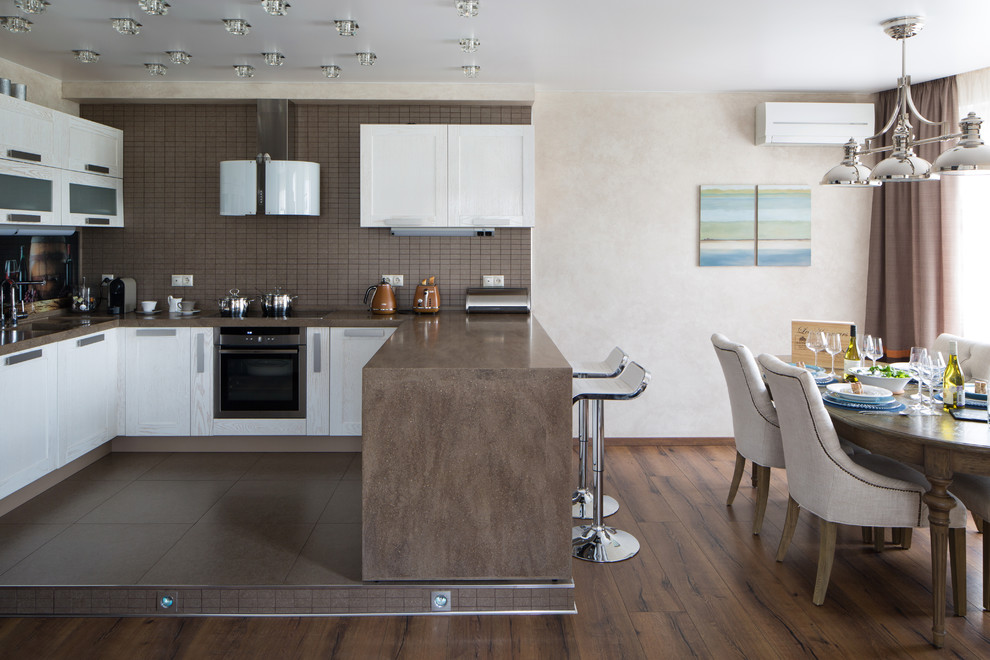 Foto på ett funkis kök, med luckor med infälld panel, vita skåp, brunt stänkskydd, rostfria vitvaror, mellanmörkt trägolv, en halv köksö och brunt golv