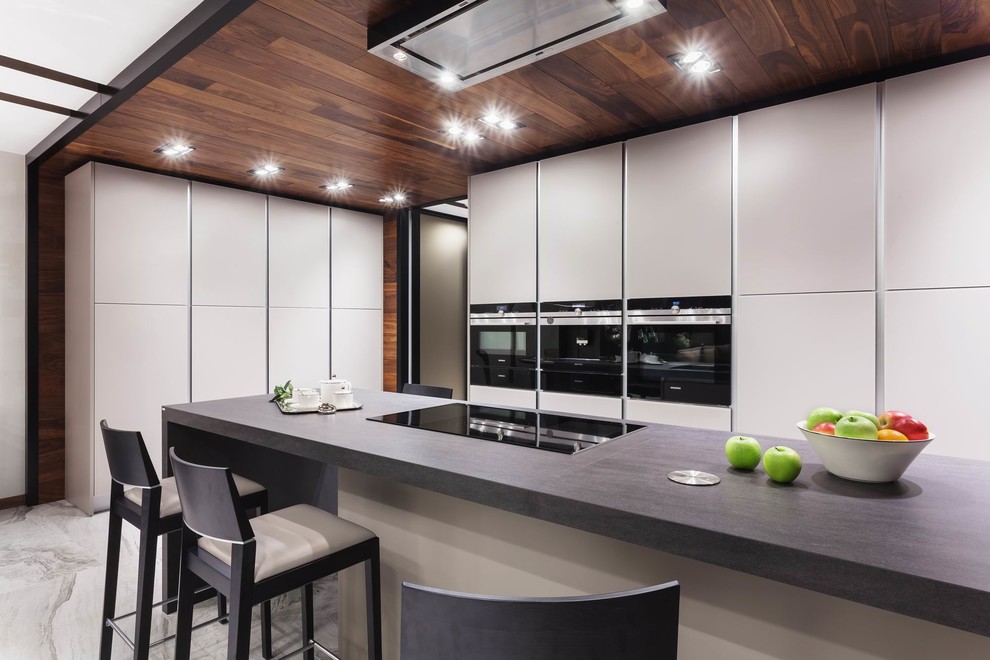 Offene Moderne Küche in L-Form mit flächenbündigen Schrankfronten, weißen Schränken, Küchengeräten aus Edelstahl und Kücheninsel in Sonstige