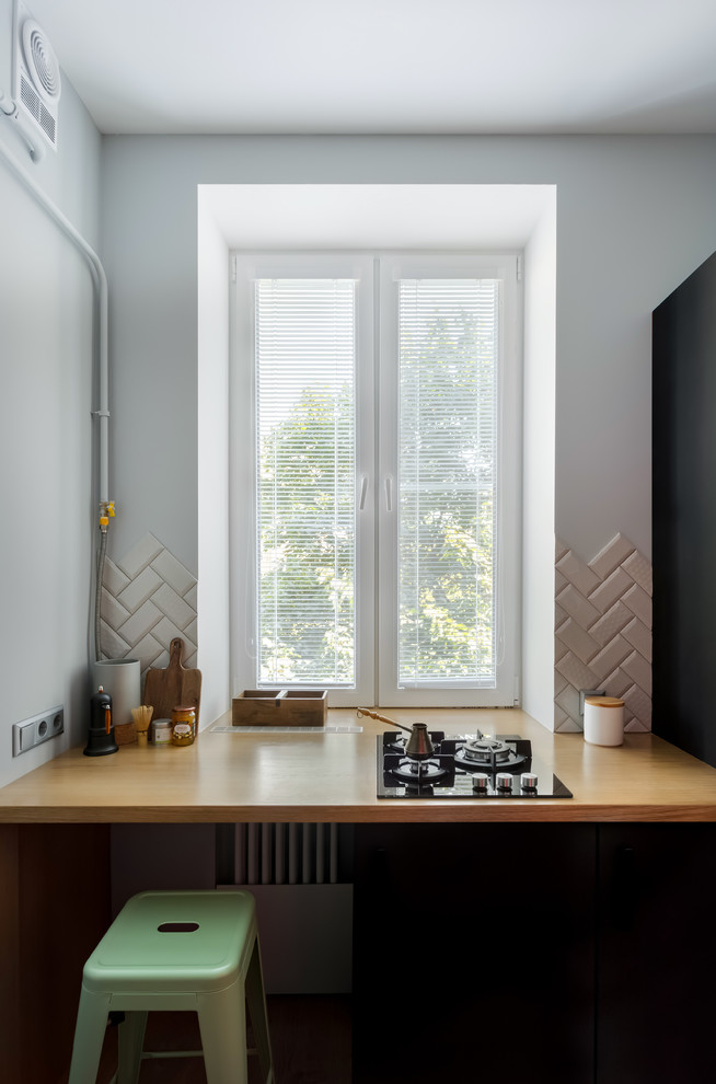 Example of a small danish galley enclosed kitchen design in Moscow with wood countertops, gray backsplash, black appliances, brown countertops and subway tile backsplash