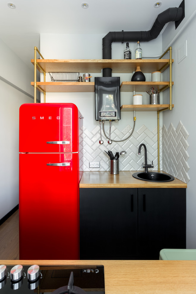 Photo of a small scandinavian galley enclosed kitchen in Moscow with flat-panel cabinets, black cabinets, wood worktops, grey splashback, laminate floors, brown floors, brown worktops, a built-in sink and metro tiled splashback.