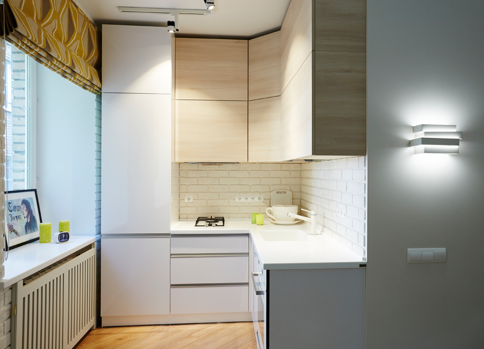 Modelo de cocinas en L contemporánea pequeña cerrada sin isla con armarios con paneles lisos, salpicadero blanco, salpicadero de ladrillos, electrodomésticos blancos y suelo de madera en tonos medios