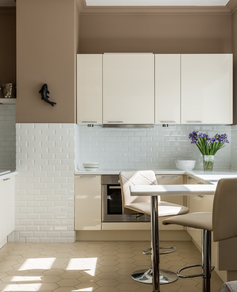 Foto di una cucina a L contemporanea con ante lisce, ante beige, paraspruzzi bianco, paraspruzzi con piastrelle diamantate, elettrodomestici in acciaio inossidabile, pavimento beige, top bianco e penisola