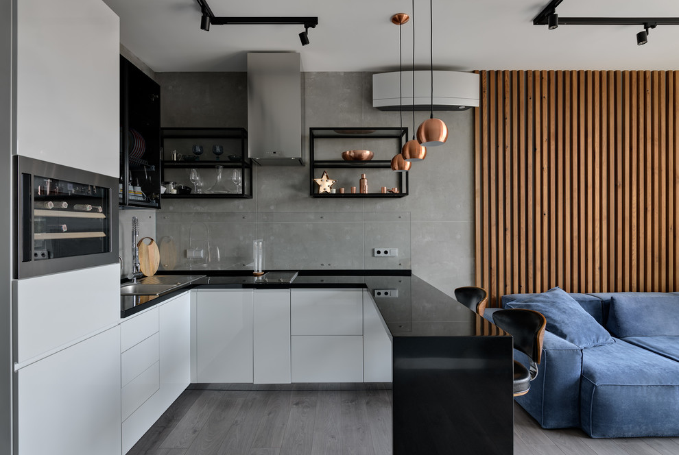 This is an example of a medium sized contemporary u-shaped open plan kitchen in Moscow with a built-in sink, flat-panel cabinets, white cabinets, engineered stone countertops, stainless steel appliances, laminate floors, grey floors and black worktops.