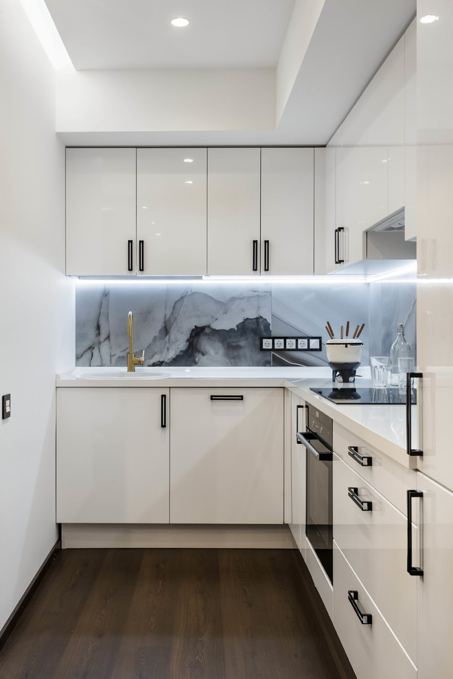 This is an example of a contemporary l-shaped open plan kitchen in Other with a built-in sink, flat-panel cabinets, white cabinets, grey splashback, stone slab splashback, black appliances, dark hardwood flooring and no island.