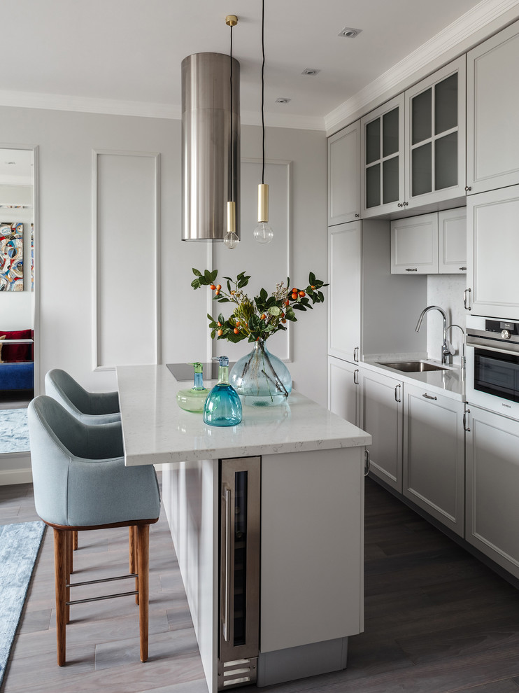 Example of a small transitional galley medium tone wood floor and gray floor kitchen design in Moscow with an undermount sink, recessed-panel cabinets, gray cabinets, quartz countertops, white backsplash, marble backsplash, stainless steel appliances, an island and white countertops