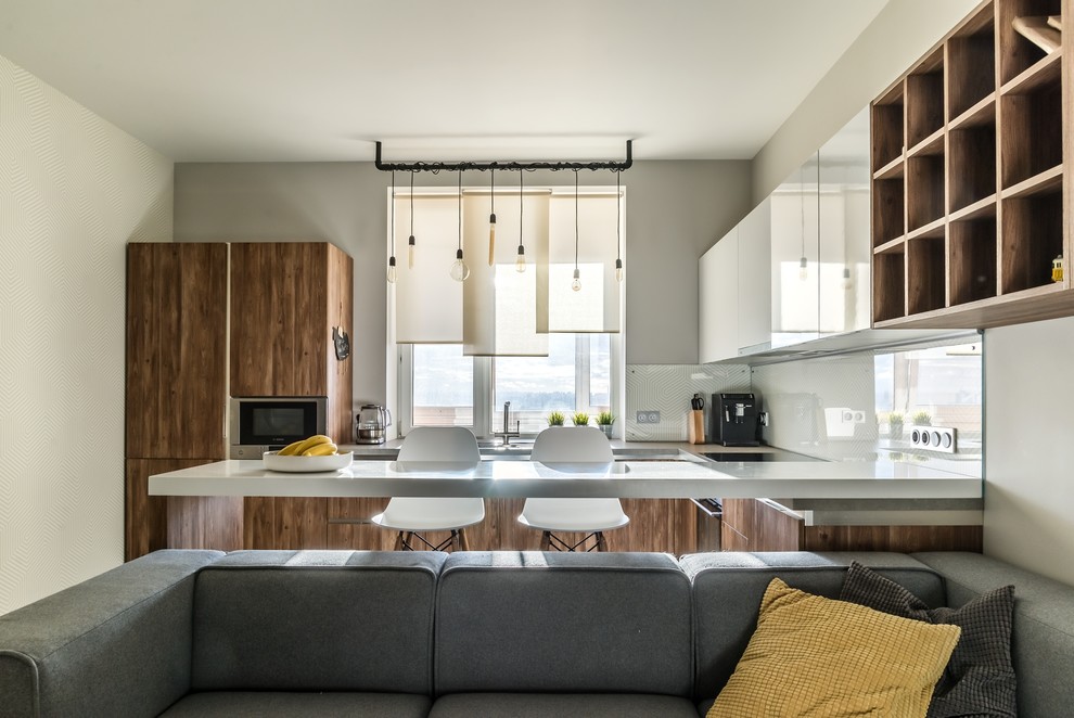 Свежая идея для дизайна: п-образная кухня-гостиная у окна в современном стиле с плоскими фасадами, темными деревянными фасадами, белым фартуком, техникой из нержавеющей стали и полуостровом - отличное фото интерьера