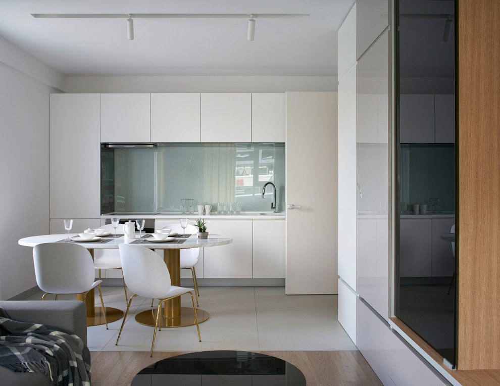 Modern inredning av ett litet, avskilt vit vitt l-kök, med en dubbel diskho, släta luckor, vita skåp, glaspanel som stänkskydd och grått golv