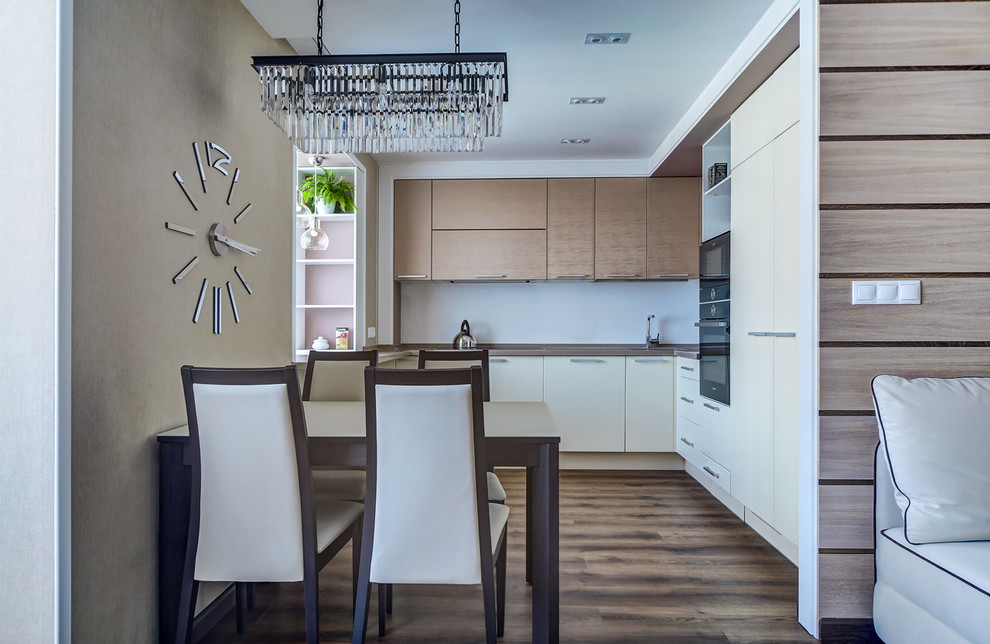 Стильный дизайн: кухня-гостиная в современном стиле с белыми фасадами, белым фартуком и коричневым полом - последний тренд