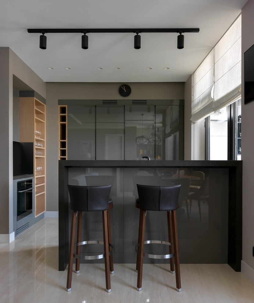 На фото: глянцевая кухня-гостиная среднего размера в современном стиле с плоскими фасадами, серыми фасадами, полуостровом и бежевым полом