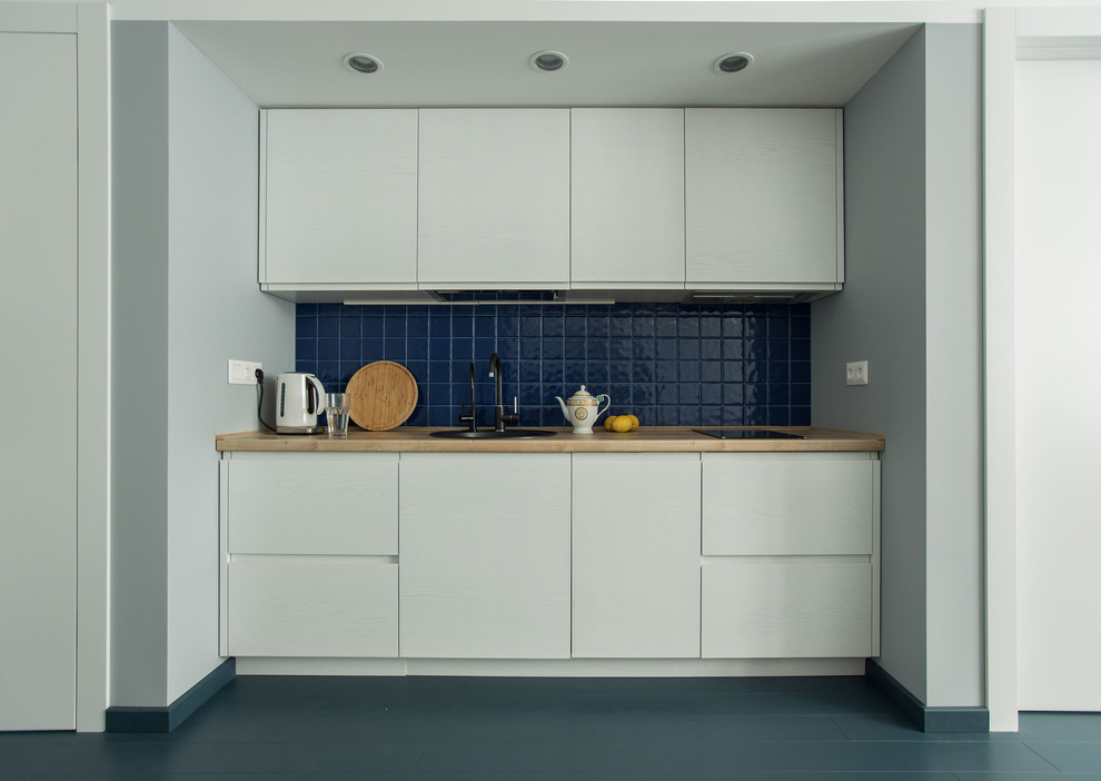 Modelo de cocina lineal actual abierta sin isla con fregadero encastrado, armarios con paneles lisos, puertas de armario blancas, salpicadero azul y suelo gris