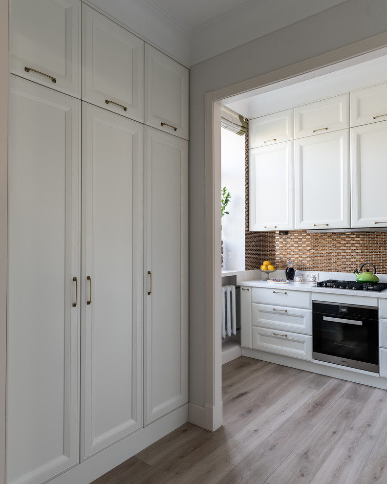 Mid-sized transitional l-shaped laminate floor and beige floor enclosed kitchen photo in Moscow with an undermount sink, raised-panel cabinets, white cabinets, solid surface countertops, yellow backsplash, mosaic tile backsplash, stainless steel appliances and white countertops