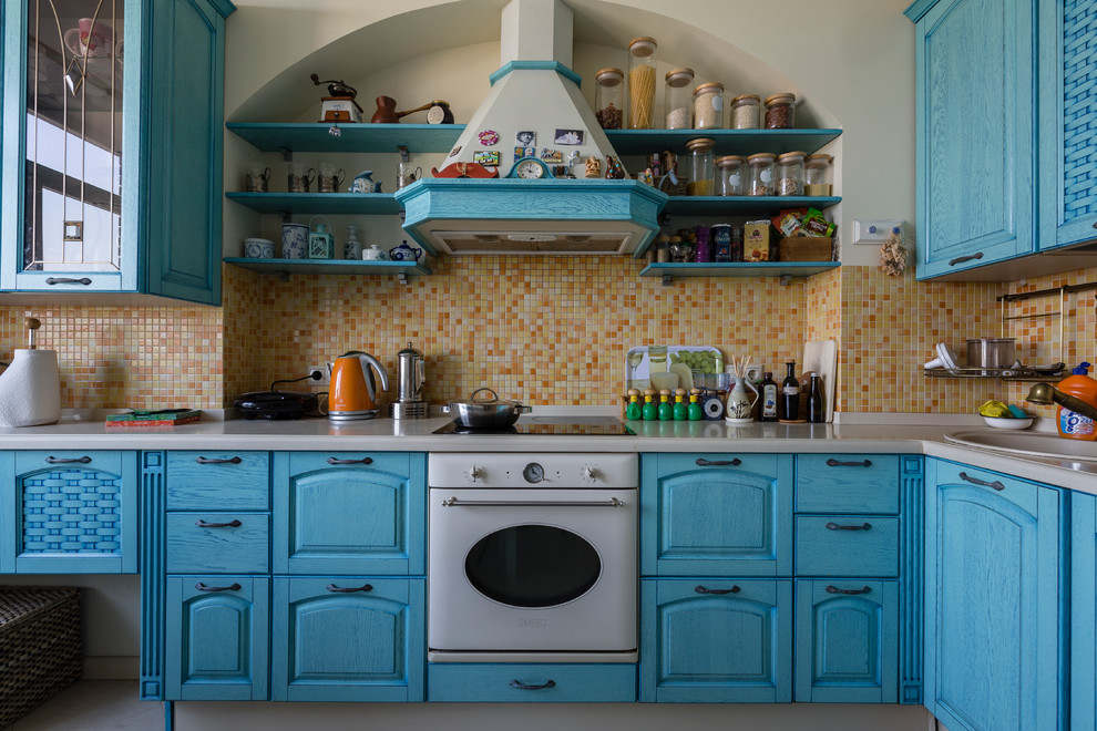 Country Küche in L-Form mit blauen Schränken, Küchenrückwand in Gelb, Rückwand aus Mosaikfliesen und weißen Elektrogeräten in Sankt Petersburg