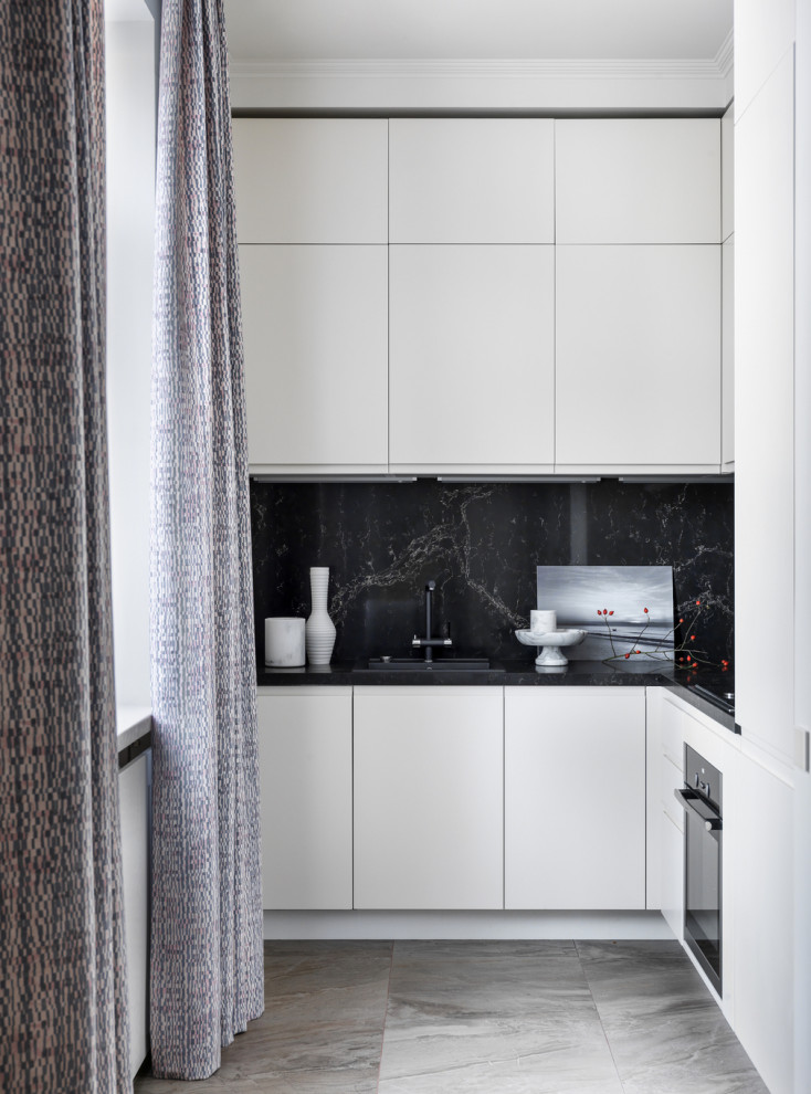 На фото: угловая кухня в современном стиле с накладной мойкой, плоскими фасадами, черным фартуком, черной техникой, серым полом, черной столешницей и черно-белыми фасадами