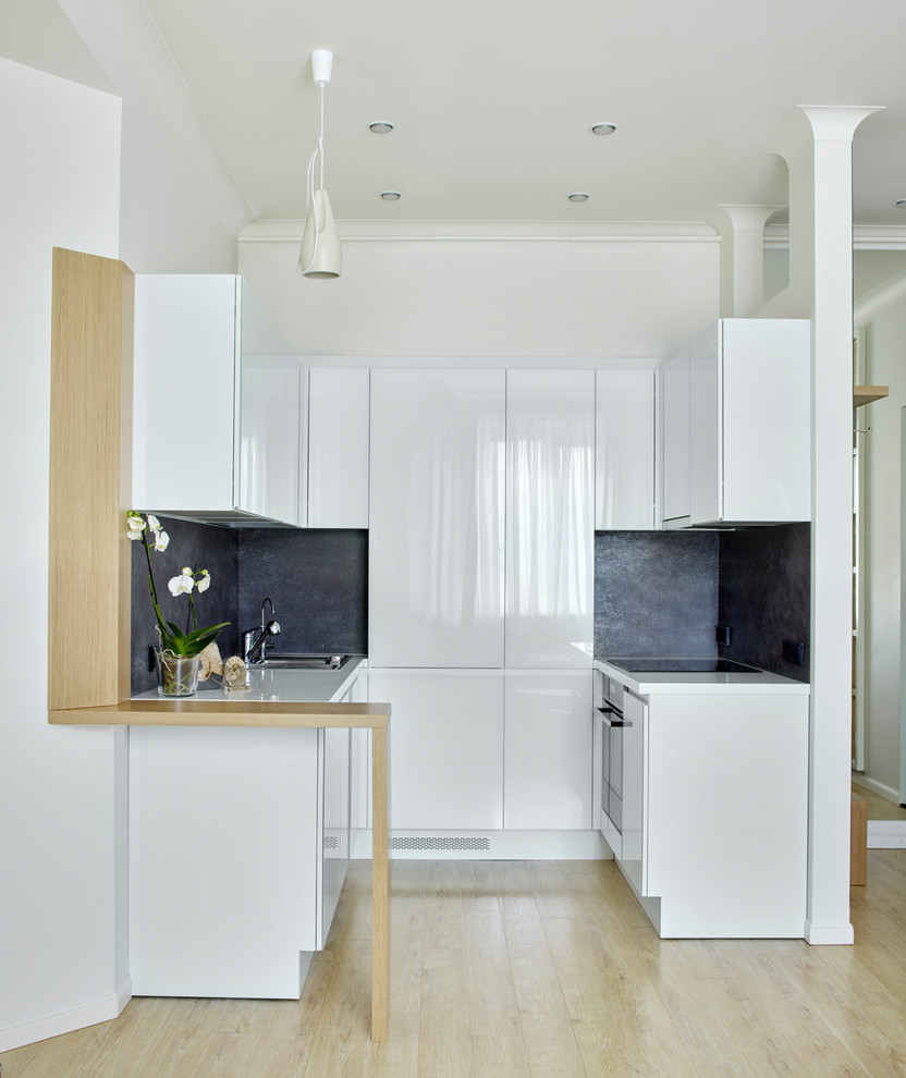 Diseño de cocina actual abierta con armarios con paneles lisos, puertas de armario blancas, salpicadero negro, suelo de madera clara, encimeras blancas y fregadero de un seno