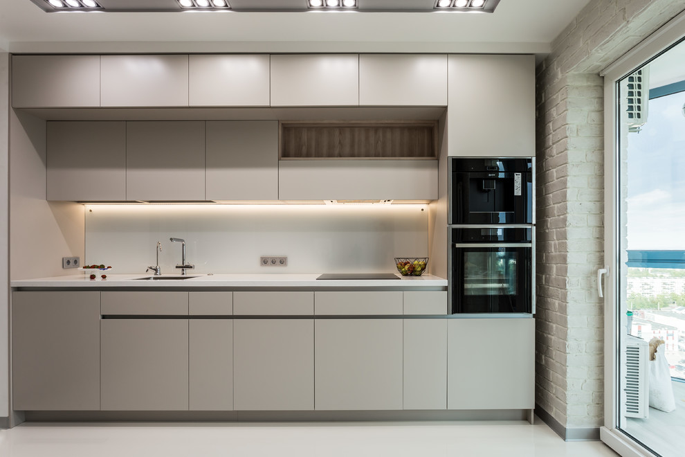 Foto på ett funkis vit linjärt kök, med släta luckor, vitt stänkskydd, glaspanel som stänkskydd, svarta vitvaror, vitt golv, en enkel diskho, beige skåp och betonggolv