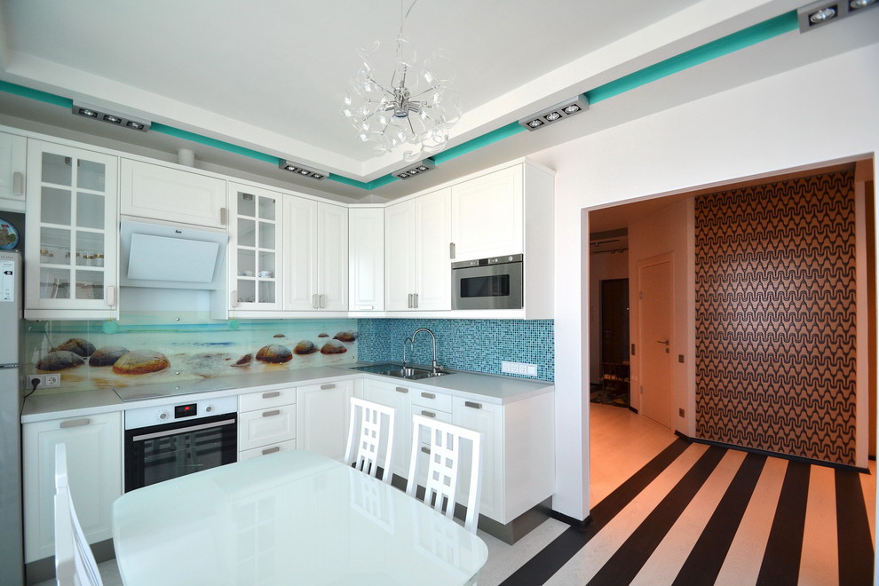 Modern inredning av ett mellanstort kök, med en nedsänkt diskho, luckor med infälld panel, vita skåp, laminatbänkskiva, blått stänkskydd, glaspanel som stänkskydd, vita vitvaror, laminatgolv och vitt golv