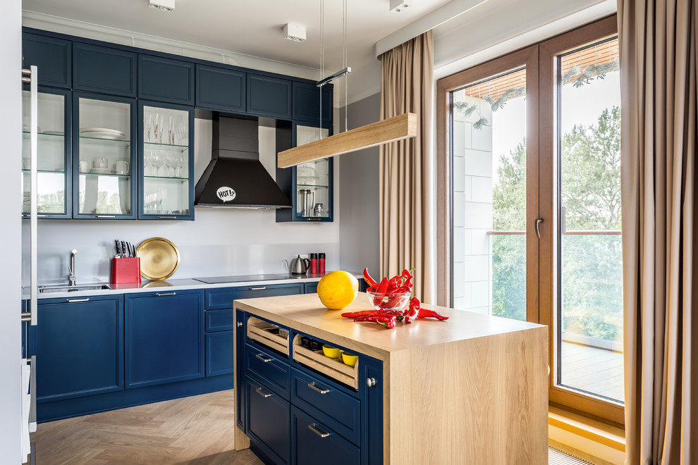 Foto di una cucina minimal di medie dimensioni con lavello sottopiano, ante a filo, ante blu, top in superficie solida, paraspruzzi bianco, elettrodomestici neri, pavimento in legno massello medio, pavimento beige e top bianco