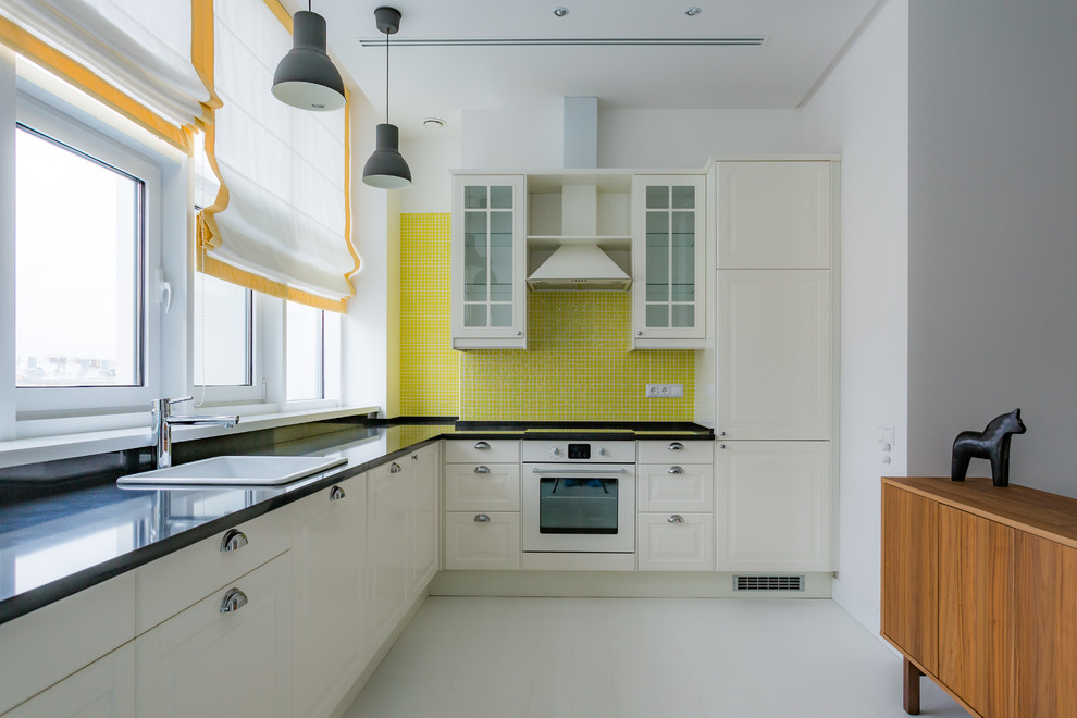 Источник вдохновения для домашнего уюта: угловая кухня-гостиная в современном стиле с накладной мойкой, фасадами с выступающей филенкой, белыми фасадами, желтым фартуком, фартуком из плитки мозаики, белой техникой и белым полом без острова