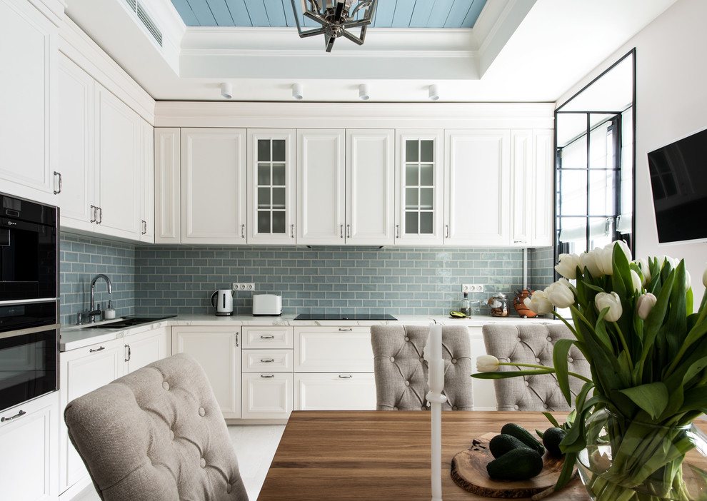 На фото: угловая кухня в стиле неоклассика (современная классика) с врезной мойкой, белыми фасадами, серым фартуком, черной техникой и белым полом с