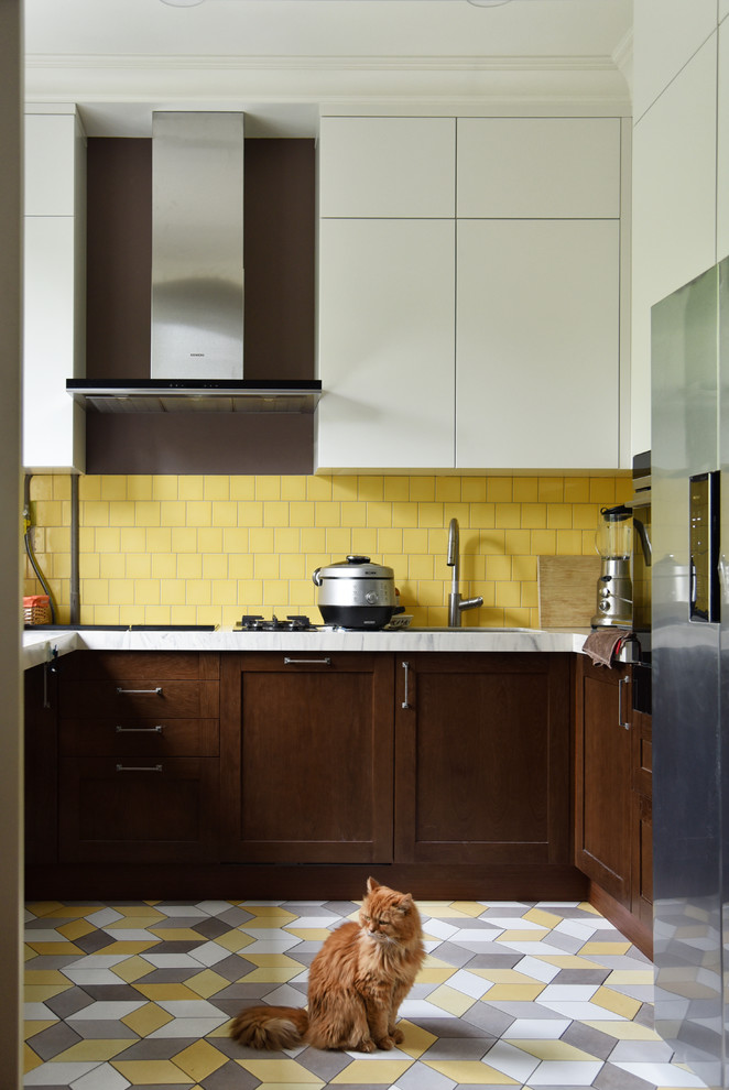 На фото: п-образная кухня-гостиная среднего размера в современном стиле с врезной мойкой, плоскими фасадами, белыми фасадами, столешницей из акрилового камня, желтым фартуком, фартуком из керамической плитки, техникой из нержавеющей стали, полом из керамической плитки, разноцветным полом и белой столешницей