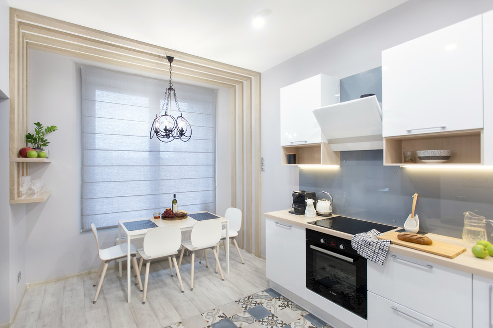 Medium sized scandinavian l-shaped kitchen/diner in Saint Petersburg with a single-bowl sink, flat-panel cabinets, white cabinets, blue splashback, glass sheet splashback, black appliances, porcelain flooring, no island, multi-coloured floors and beige worktops.