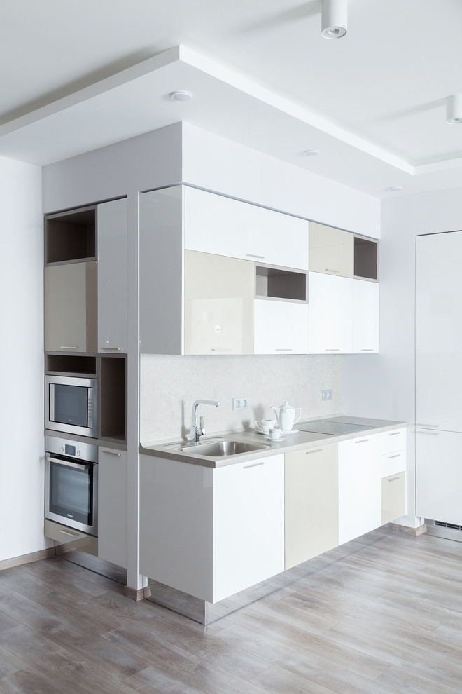 Свежая идея для дизайна: угловая кухня-гостиная среднего размера в современном стиле с плоскими фасадами, белыми фасадами, бежевым фартуком и паркетным полом среднего тона - отличное фото интерьера