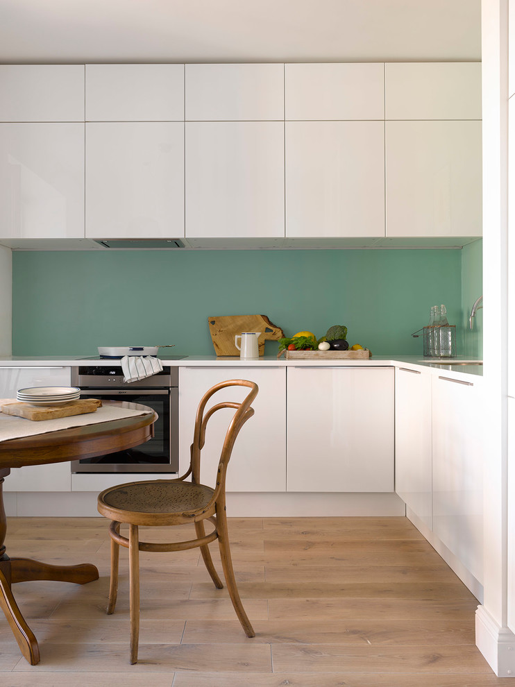Inspiration for a scandi l-shaped enclosed kitchen in Moscow with a submerged sink, flat-panel cabinets, white cabinets, stainless steel appliances, light hardwood flooring, no island, beige floors and white worktops.