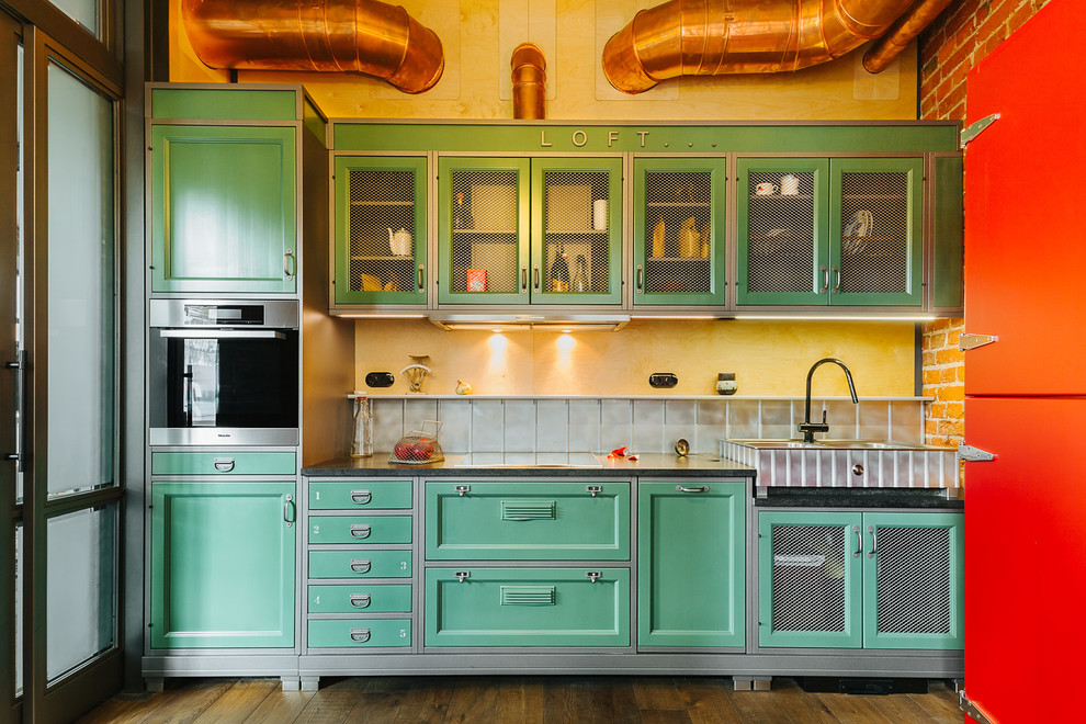 Immagine di una cucina lineare industriale con lavello stile country, ante con riquadro incassato, ante verdi, elettrodomestici in acciaio inossidabile, pavimento marrone e top nero