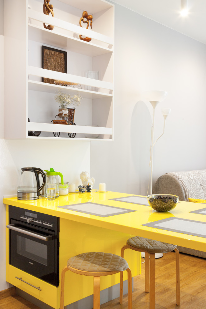 Moderne Wohnküche mit schwarzen Elektrogeräten, braunem Holzboden, Halbinsel, gelber Arbeitsplatte, gelben Schränken, flächenbündigen Schrankfronten und braunem Boden in Jekaterinburg