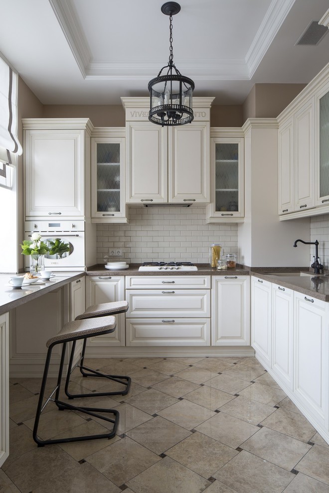 Klassisk inredning av ett kök, med en undermonterad diskho, luckor med upphöjd panel, vita skåp, vitt stänkskydd, vita vitvaror och beiget golv