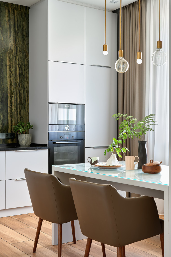 Imagen de cocina comedor contemporánea con armarios con paneles lisos, puertas de armario grises, electrodomésticos negros, suelo de madera clara, suelo beige y encimeras negras