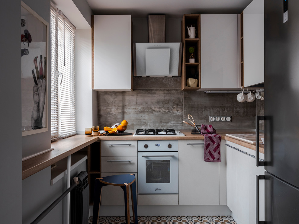 Bild på ett litet, avskilt funkis brun brunt l-kök, med en nedsänkt diskho, släta luckor, vita skåp, träbänkskiva, grått stänkskydd, vita vitvaror och flerfärgat golv